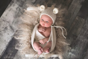 awake wrapped baby wearing a bear hat at his newborn session in barrie ontario