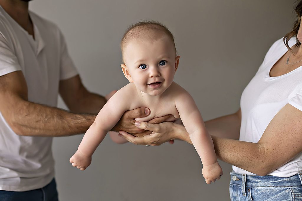 Smiling baby held by parents in casual white shirts