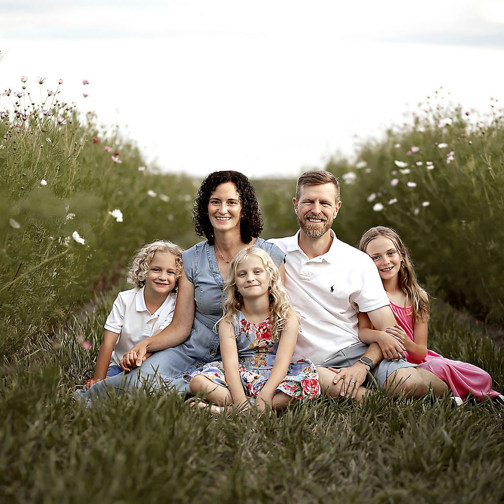 Family of five sitting in lush flower field during summer