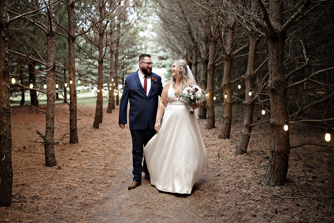 Bride and groom holding hands in forested pathway