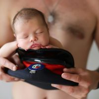 Newborn sleeping in RCMP hat held by shirtless man