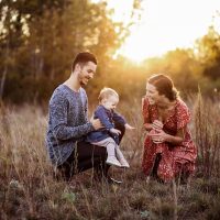 Happy family in meadow at sunset with parents kneeling beside their child