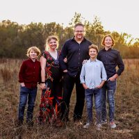 Family of five smiling in a grassy field at sunset