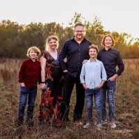 Family of five smiling in a grassy field at sunset