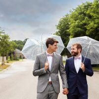 Happy couple holding umbrellas and walking on a tree-lined street