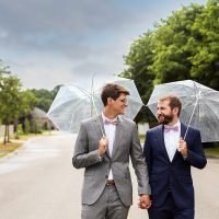 Happy couple holding umbrellas and walking on a tree-lined street